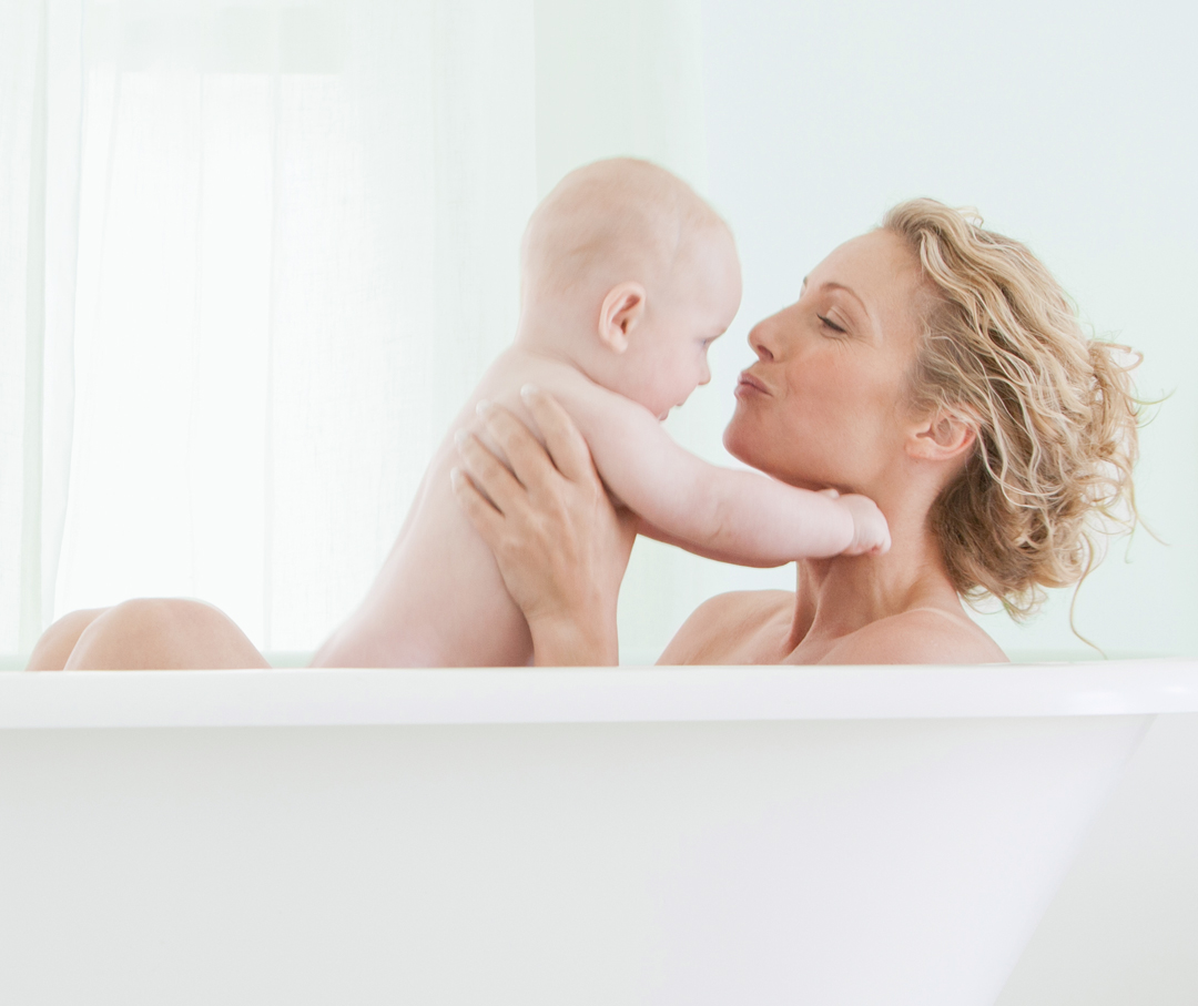 Woman and a baby in a tub playing around.