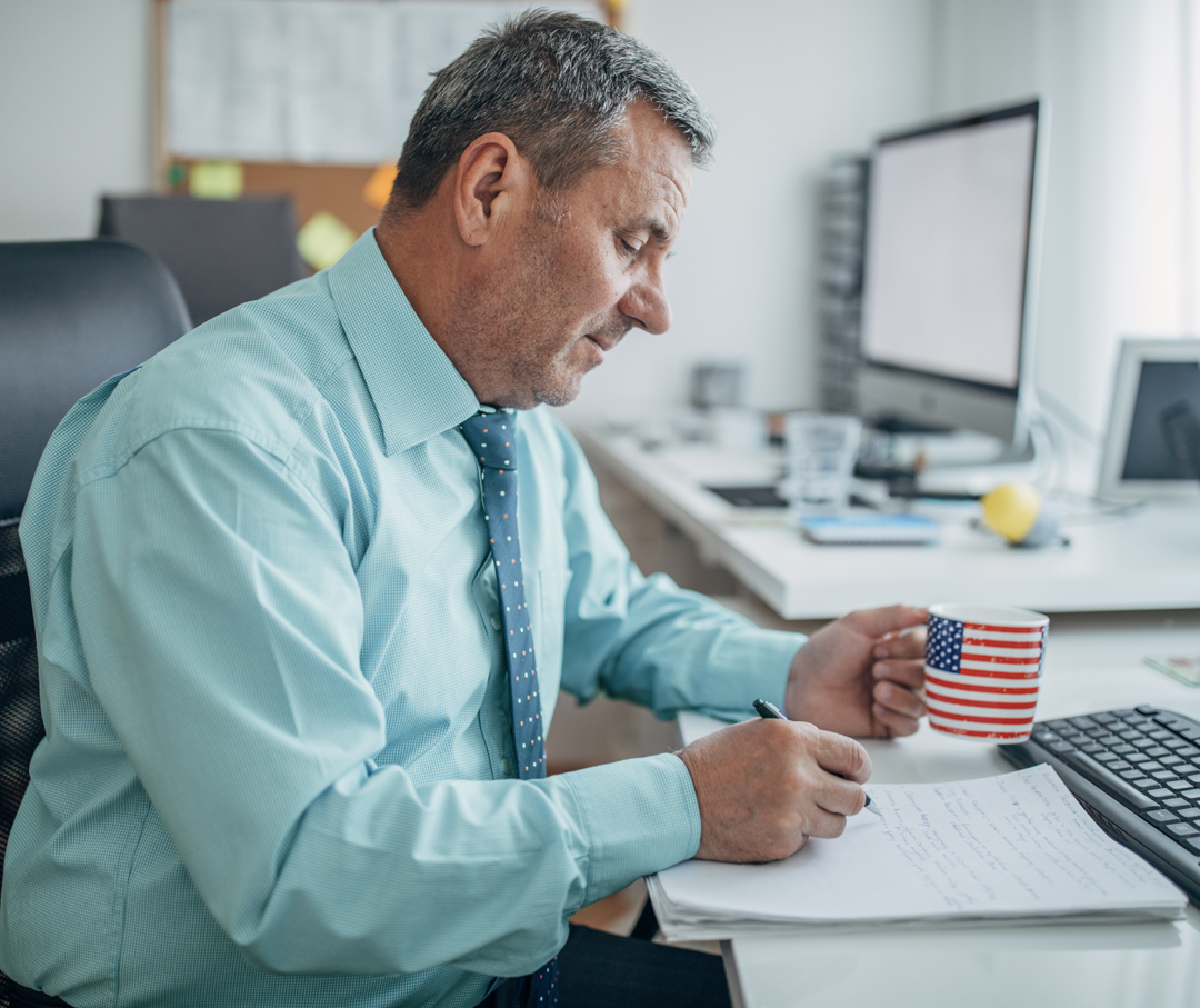 Image of a man reviewing reports drinking coffee.
