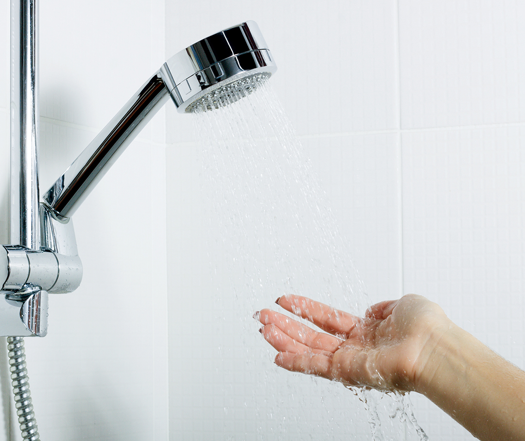 Hand help shower head spraying down in a hand for water check.